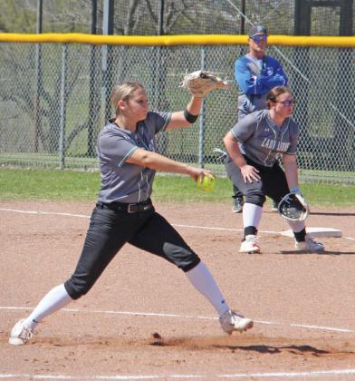 Dublin Lady Lion pitcher Jaylee Black kicks up dirt as she winds up a pitch during the March 11 home game against Peaster. Chloey Rollins stands poised at first base in the back. Paul Gaudette | Citizen staff photo