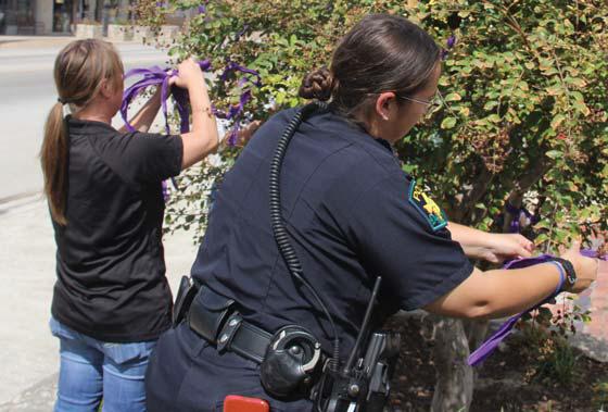 Officer Kristi Bonilla and Police Department Administrative Assistant Kayla Splawn tie purple ribbons to trees at the Corner Lot in honor of Domestic Violence Awareness Month. Wyndi Veigel | Citizen staff photo