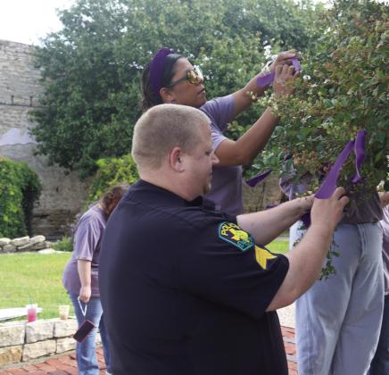 Local police officers, volunteers and employees with Cross Timbers Family Services tie purple ribbons to the trees at the Corner Lot in honor of Domestic Violence Awareness Month. Wyndi Veigel-Gaudette | Citizen staff photo
