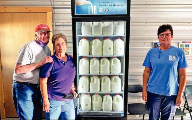 The Love Basket organizers Ray and Barbara Sissom pose with local dairy owner Linda Beukeboom by a refrigerated case and whole milk donated so that patrons of the food pantry can get the nutrition that the beverage provides. | submitted photo