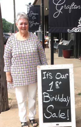 Trudy Spears poses next to a board announcing her store's first anniversary