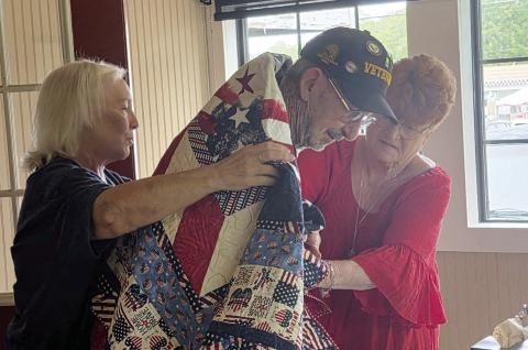 Veteran and longtime U.S. postal worker Ray LaBaume receives a Quilt of Valor from Quilters Judy Angle and Peggy DeLaVergne. Wyndi Veigel-Gaudette | Citizen staff photo